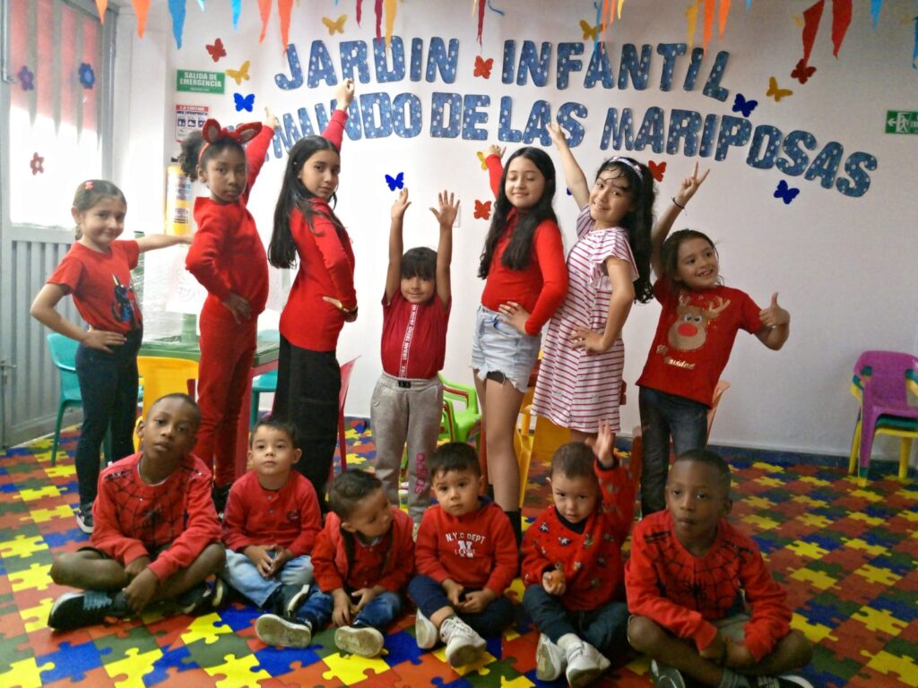 Grupo de niños vestidos de rojo interactuando en un jardín Montessori, con juguetes y herramientas educativas.