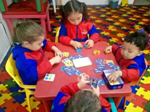 Niños en un aula Montessori jugando con bloques de colores y tarjetas, fomentando su aprendizaje autónomo y habilidades sociales.