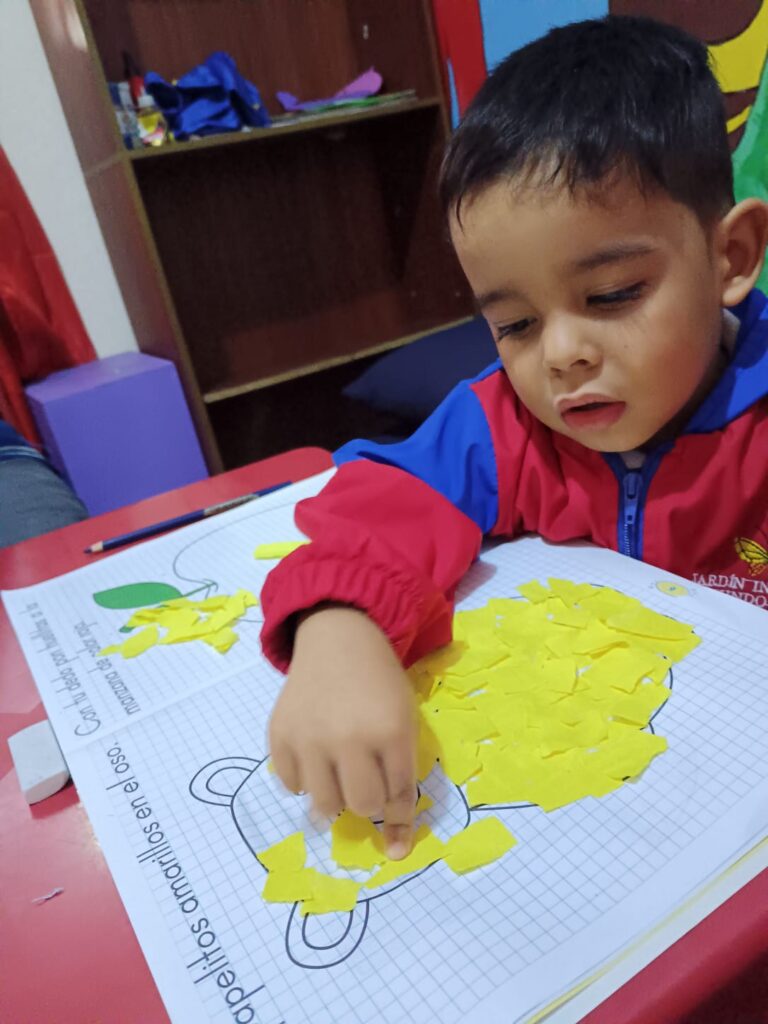 Un niño haciendo una actividad de rasgar y pegar pedazos de papel amarillo sobre un molde.