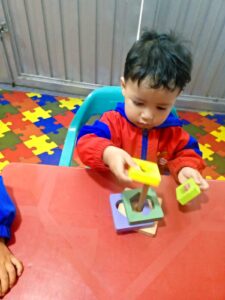 Niño pequeño manipulando un juguete apilable en un aula Montessori, fomentando su aprendizaje y desarrollo de habilidades motoras.