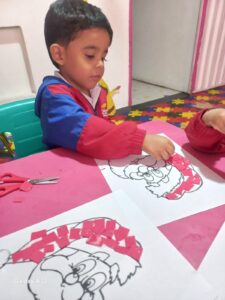 Estudiante del Jardín Infantil Montessori en Engativá realizando actividad de motricidad fina, concentrado en recortar y pegar papel rosado sobre dibujo en ambiente preparado con piso de rompecabezas multicolor